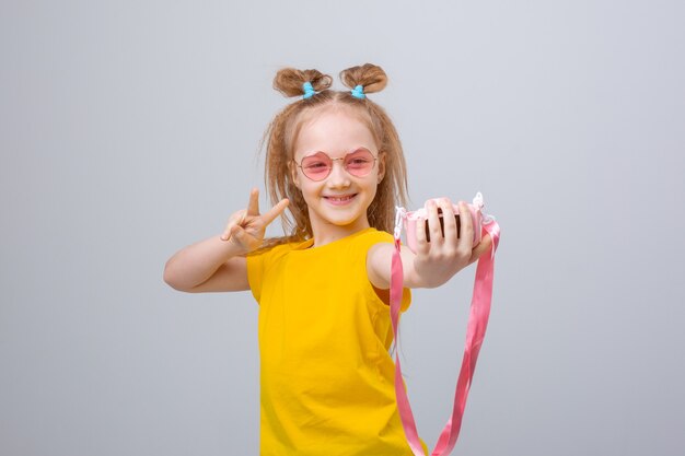 Petite fille à lunettes de soleil voyageur est titulaire d'un appareil photo sur fond blanc