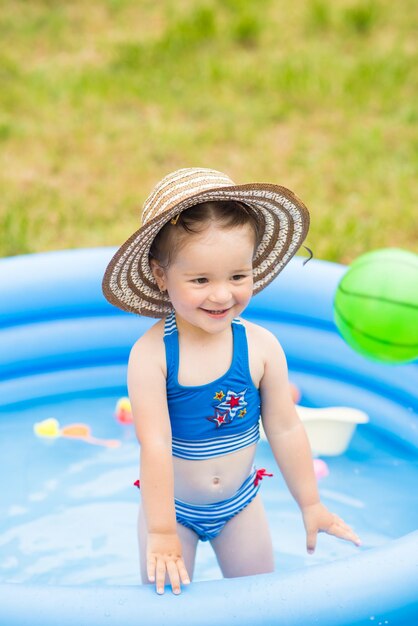 Petite fille en maillot de bain jouant et nageant dans une piscine gonflable sur une pelouse dans le jardin