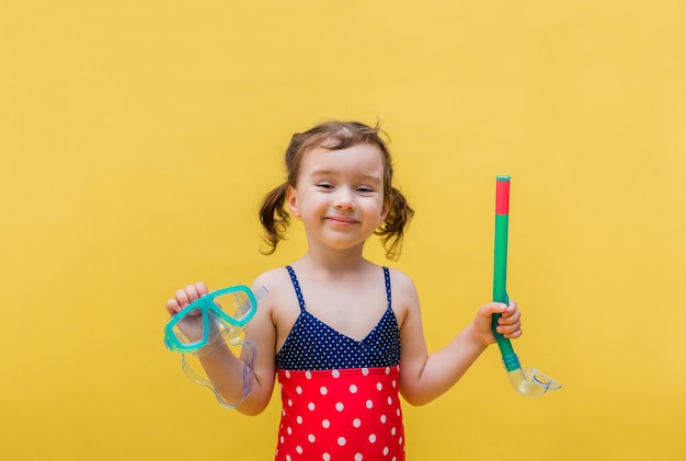 Une petite fille en maillot de bain avec un masque et un tube sur un jaune isolé