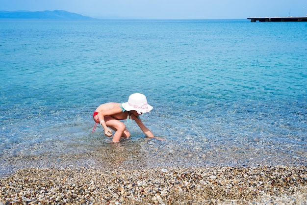 Petite fille en maillot de bain ramasse des cailloux dans la mer