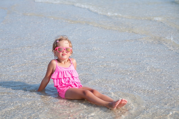 Petite fille en maillot de bain rose et lunettes de soleil à la mer