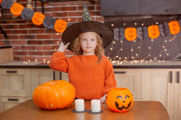 Petite fille à la maison dans la cuisine à la table avec une citrouille pour halloween