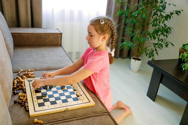 petite fille à la maison jouant avec des dames et des pièces d'échecs