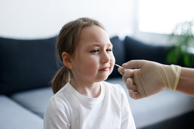 Petite Fille à La Maison Lors De La Prise D'un échantillon De Test De Mucus Nasal Du Nez Effectuant Une Procédure De Test De Virus Respiratoire Montrant Covid-19