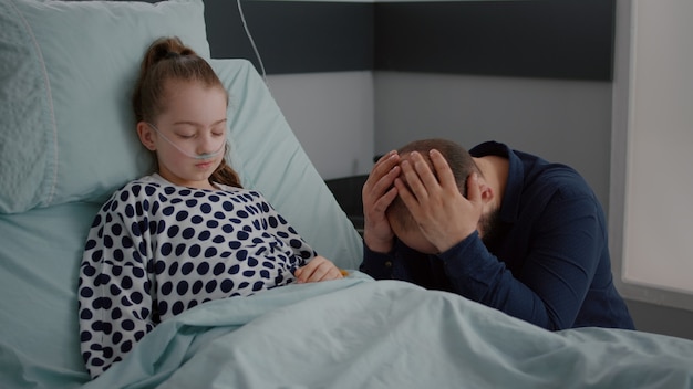 Petite fille malade avec tube nasal à oxygène allongée dans son lit dormant pendant l'examen de récupération