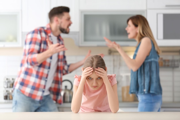 Photo petite fille malheureuse assise à table pendant que les parents se disputent la cuisine