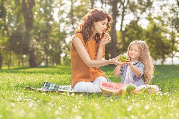 Petite fille avec maman ayant des fruits en pique-nique dans le parc