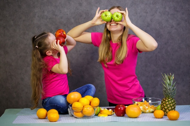 Petite fille avec maman joue avec des fruits et souriante. Vitamines et alimentation saine pour les enfants.