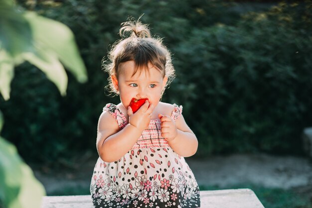 Une petite fille mange une tomate. Rétro-éclairage très mignon dans le jardin par vous-même