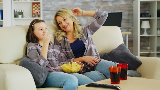 Petite fille mangeant des chips en regardant un film à la télévision avec sa mère. Mère et fille se détendre.