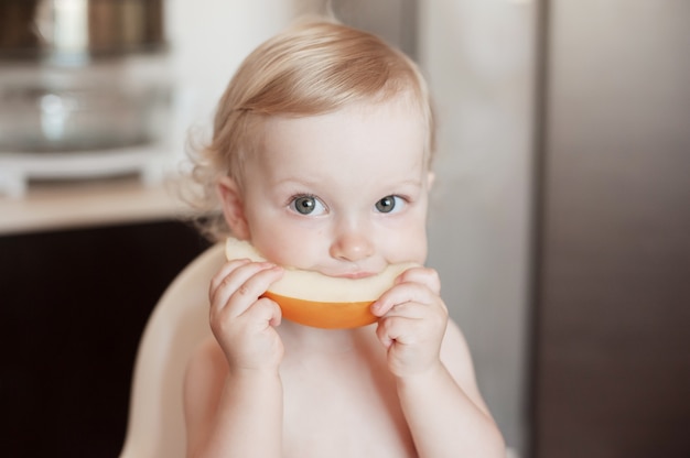 Petite fille mangeant du melon miel. Drôle enfant qui rit dans la cuisine.