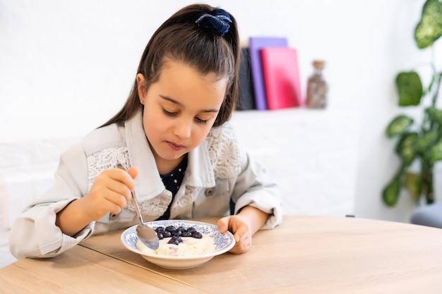 petite fille mangeant du porridge aux bleuets à table à la maison dans la cuisine