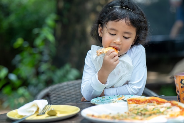 Petite fille mangeant un morceau de pizza en plein air