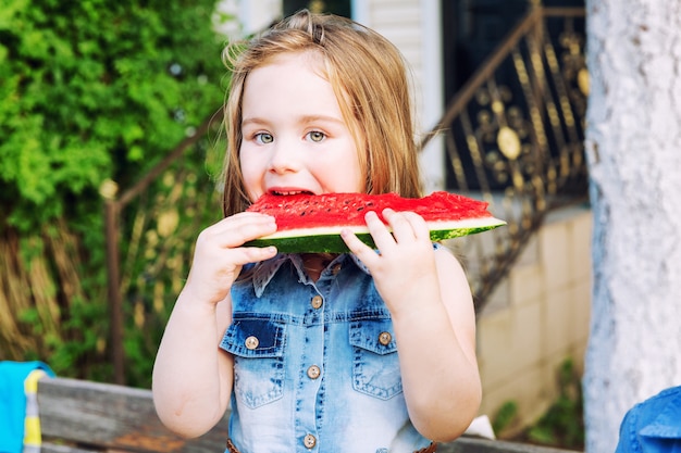 Petite fille mangeant une pastèque dans le jardin