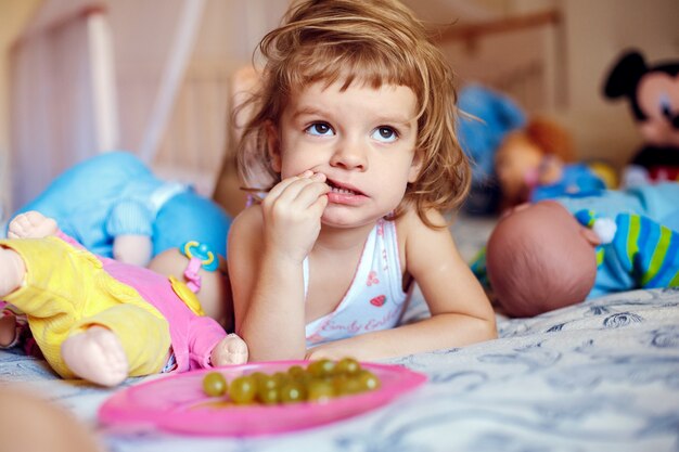 Petite fille mangeant des raisins sur le lit