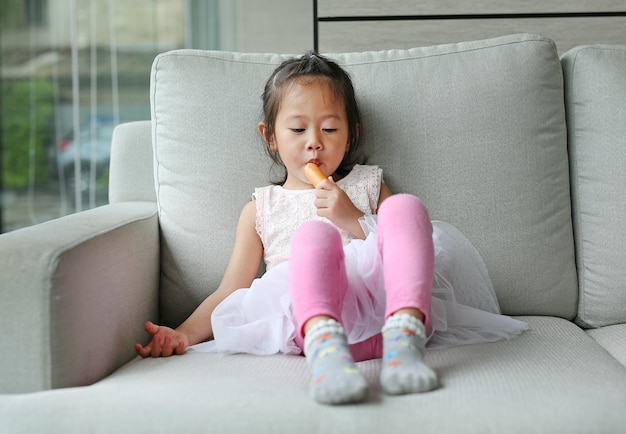 Petite fille mangeant des saucisses sur le canapé