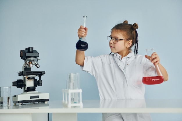 Petite fille en manteau jouant un scientifique en laboratoire à l'aide d'équipement