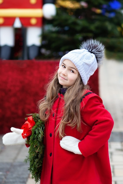 Petite fille en manteau rouge avec guirlande de Noël