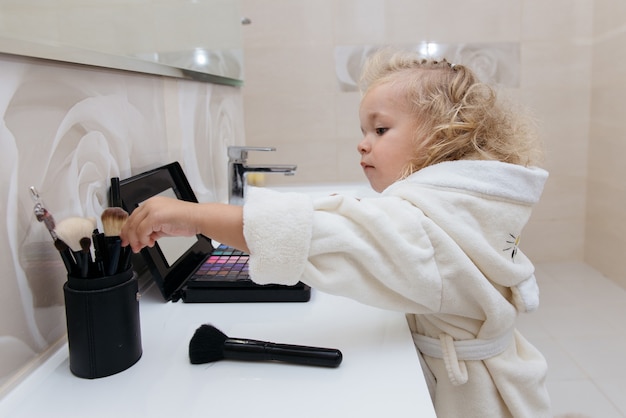 Petite fille maquillant avec des ombres à paupières en peignoir