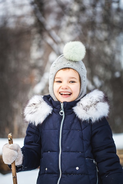 Petite fille marchant dans la forêt d'hiver dans une veste bleue et un chapeau gris