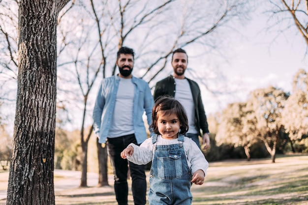 Une petite fille marchant dans le parc suivie de ses parents Concept de famille gay