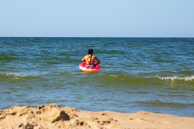 Petite fille sur la mer avec une bouée de sauvetage rose un jour d'été, vacances