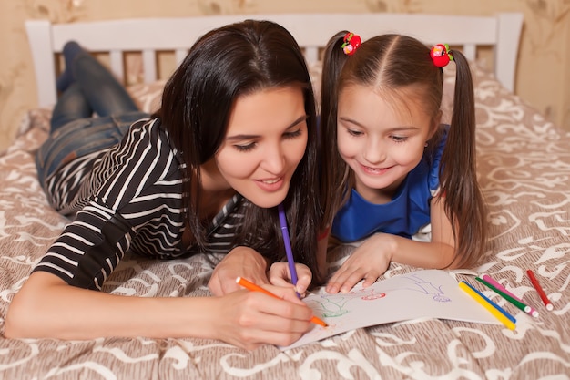 La petite fille et la mère dessinent allongées sur un lit.