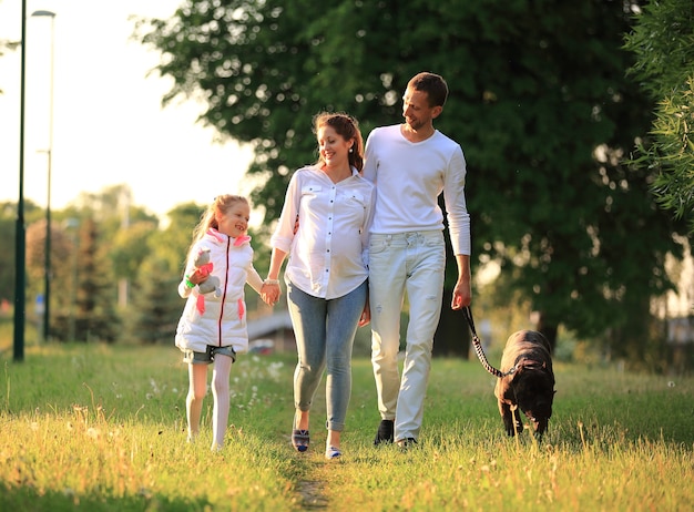 Petite fille avec une mère enceinte, un père heureux et un chien pour une promenade dans le parc un jour de printemps