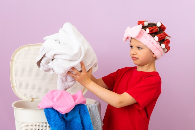 Une petite fille met du linge sale dans le panier. Nettoyage à domicile et blanchisserie.