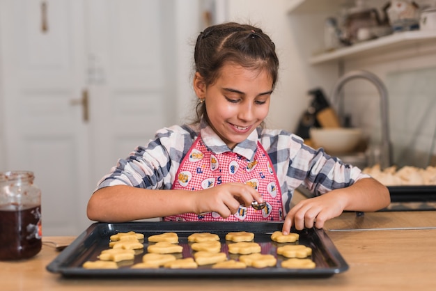 Photo petite fille mettant de la confiture sur les cookies dans un plateau.