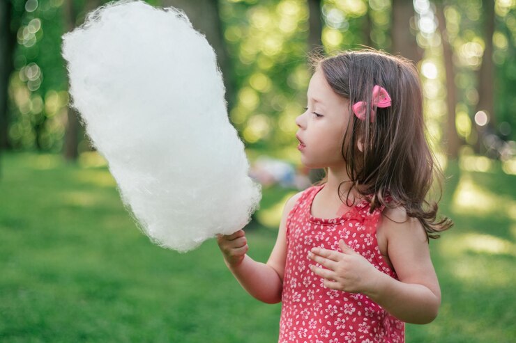 Petite fille mignonne 3-4 mangeant de la barbe à papa dans un parc ensoleillé, parmi de grands arbres sur l'herbe verte