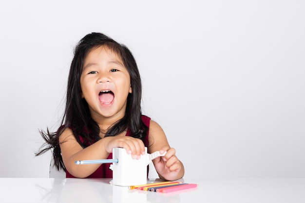 Petite fille mignonne de 3 ans sourit à l'aide d'un taille-crayon tout en faisant ses devoirs