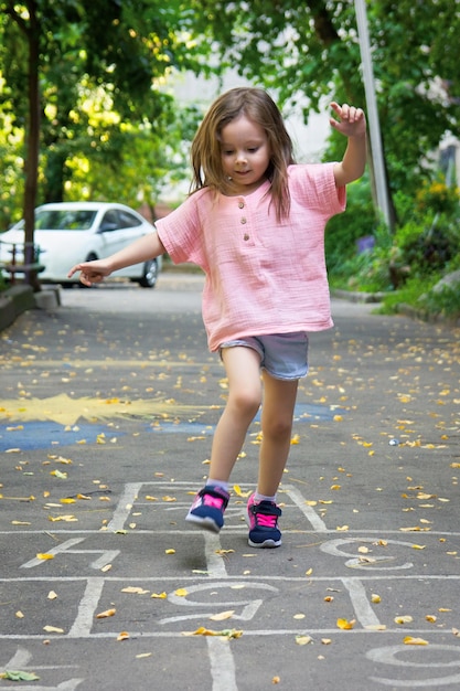 Petite fille mignonne de 4 ans jouant à la marelle sur l'aire de jeux à l'extérieur Soft focus sélectif Vertical