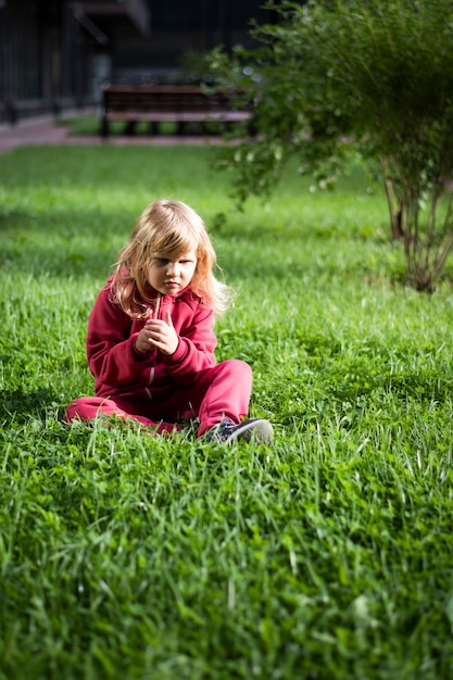 Petite fille mignonne 5 ans blonde en vêtements rouges sur l'herbe