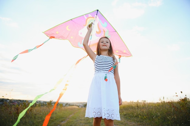 Petite fille mignonne de 7 ans courant sur le terrain avec un cerf-volant le jour d'été