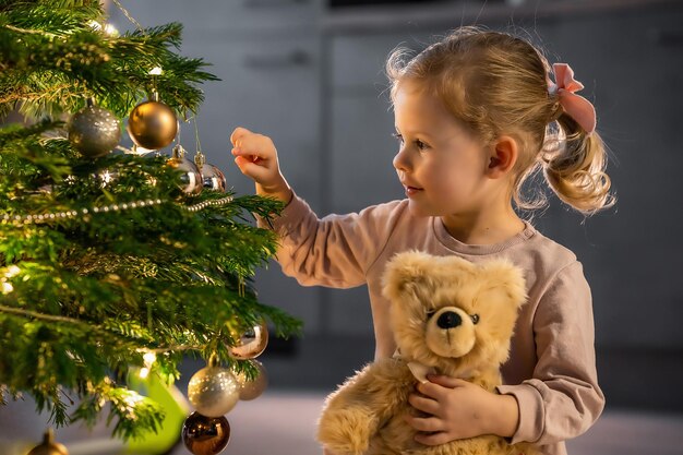 Une petite fille mignonne accrochant des boules sur l'arbre de Noël à la maison