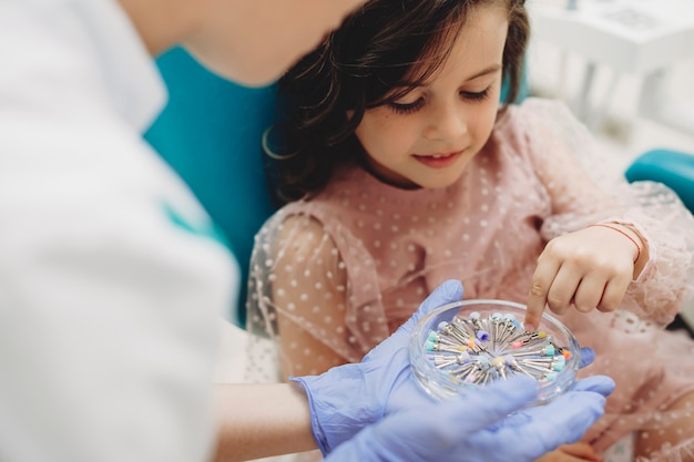 Petite fille mignonne aidant la stomatologie pédiatrique à choisir un instrument pour la chirurgie des dents.