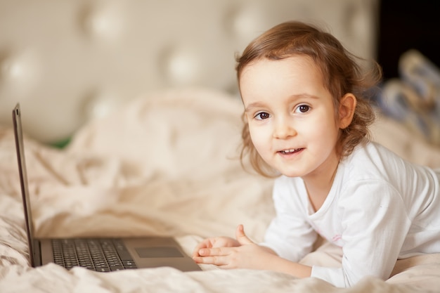 Petite fille mignonne allongée sur le lit et à l'aide d'un ordinateur portable numérique