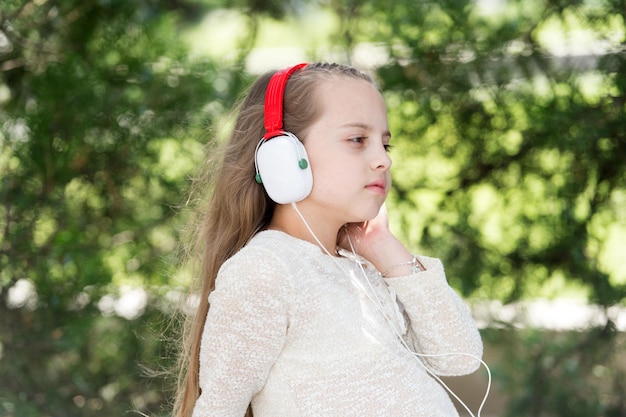 Petite fille mignonne appréciant la musique utilisant des écouteurs au jour d'été