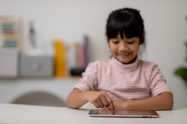 Petite fille mignonne asiatique touchant l'écran de la tablette numérique sur la table