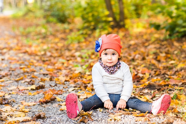 Petite fille mignonne assise dans un tas de feuilles jaunes.