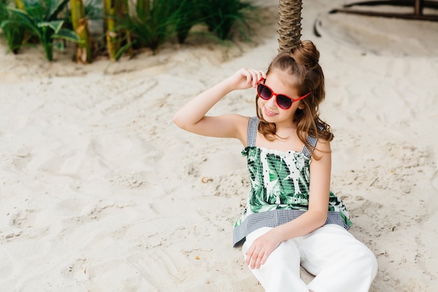 Petite fille mignonne assise sur le sable et appréciant