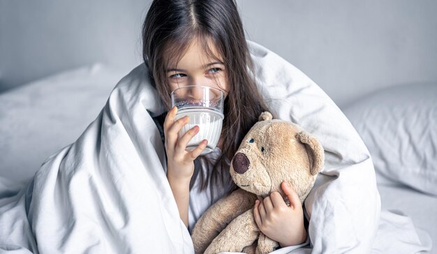 Une petite fille mignonne au lit avec une peluche et un verre de lait