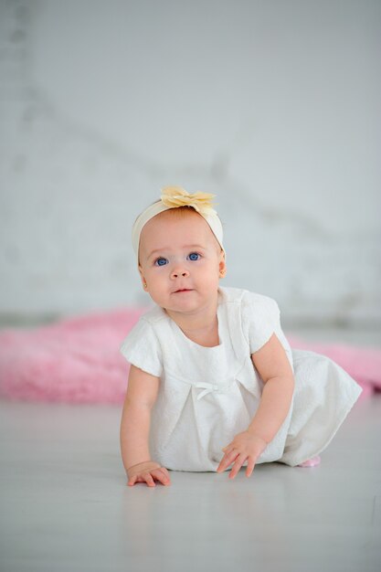 Petite fille mignonne aux grands yeux bleus. La jeune fille est vêtue d'une robe blanche. Fille apprenant à ramper.