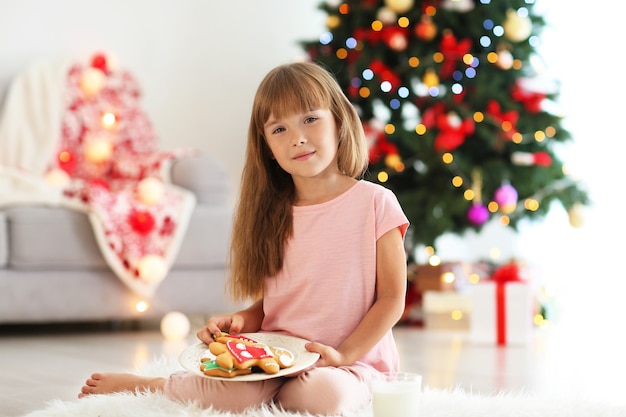 Petite fille mignonne avec des biscuits dans la chambre décorée pour Noël