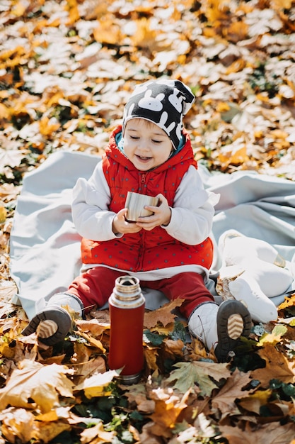 Petite fille mignonne boit du thé à partir d'un thermos dans le parc d'automne mignon petit bébé en bas âge avec thermos