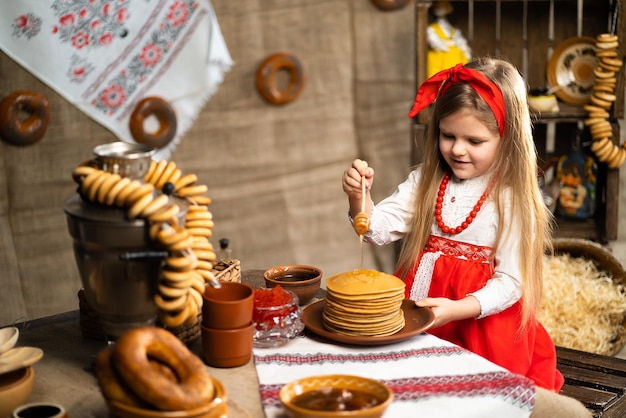 Petite fille mignonne en costume folklorique arroseurs de crêpes au miel tout en célébrant Shrovedite