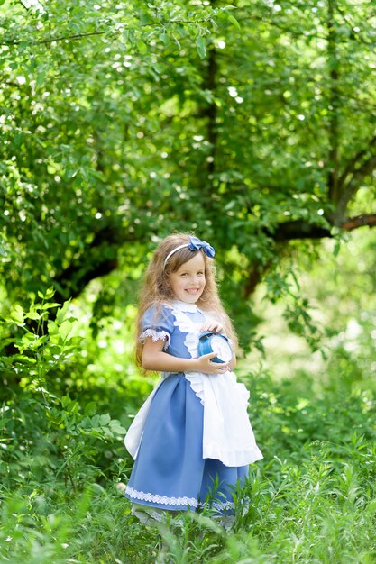 Petite fille mignonne dans un costume d'Alice tient une vieille horloge antique.