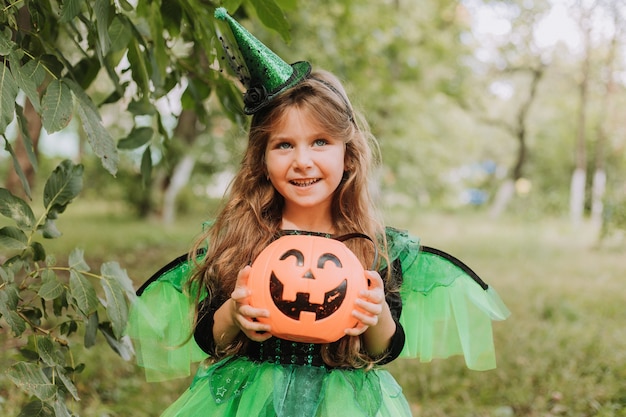 Petite fille mignonne dans un costume vert d'Halloween d'une sorcière ou d'une fée avec un panier de citrouille pour des bonbons