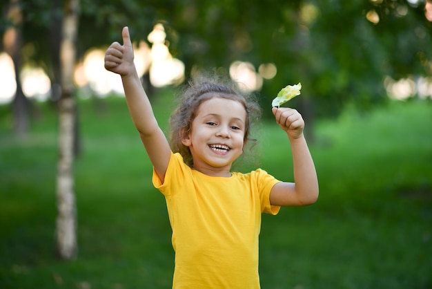 Une petite fille mignonne dans un T-shirt jaune sur fond d'arbres verts.